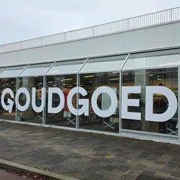 Witte letters van winkelnaam op glazen gevel met kantoorgebouw erboven
