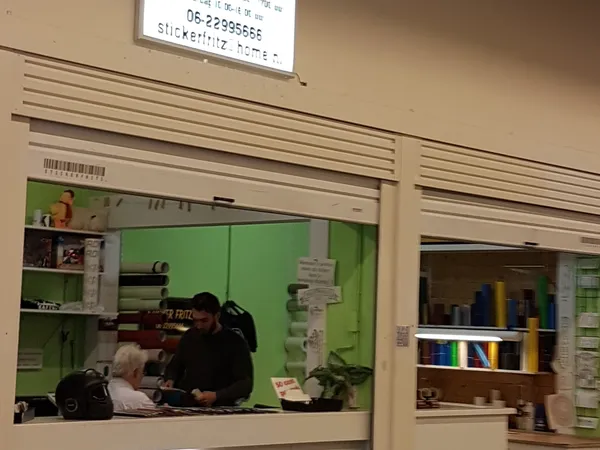 Binnenaanzicht van een kringloopwinkel met groene wanden, stellingen en een persoon achter de balie