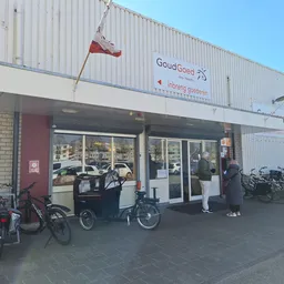 Voorgevel van kringloopwinkel GoudGoed met ingang, etalageruiten en fietsen ervoor