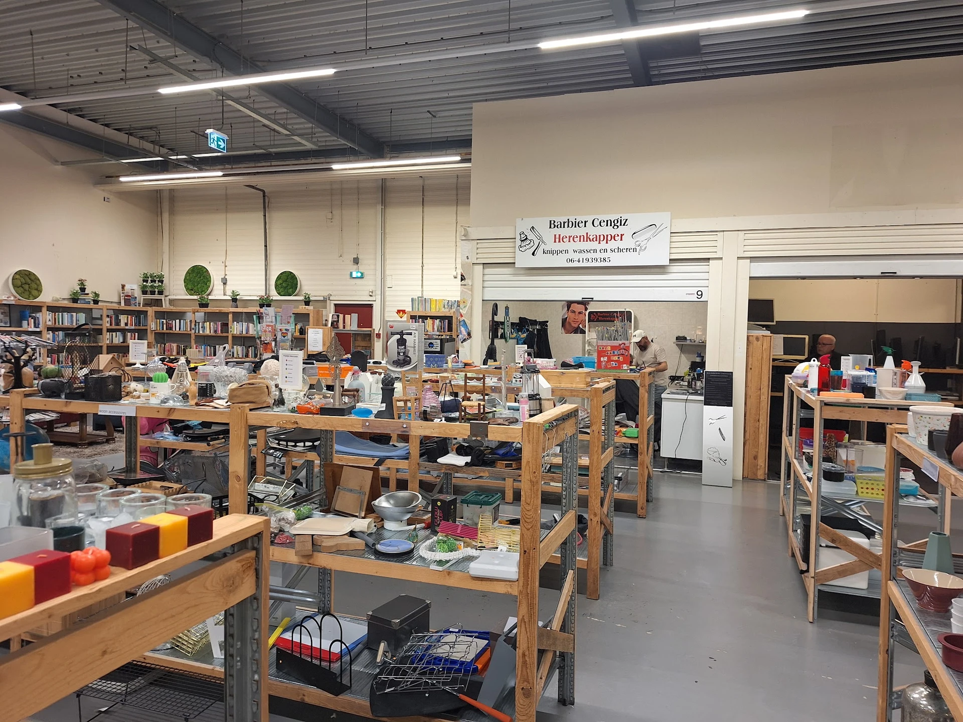 Binnenaanzicht van kringloopwinkel met houten werkafels, stellingen, boeken en diverse gebruikte spullen