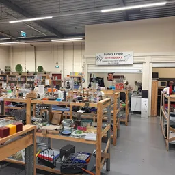 Binnenaanzicht van kringloopwinkel met houten werkafels, stellingen, boeken en diverse gebruikte spullen