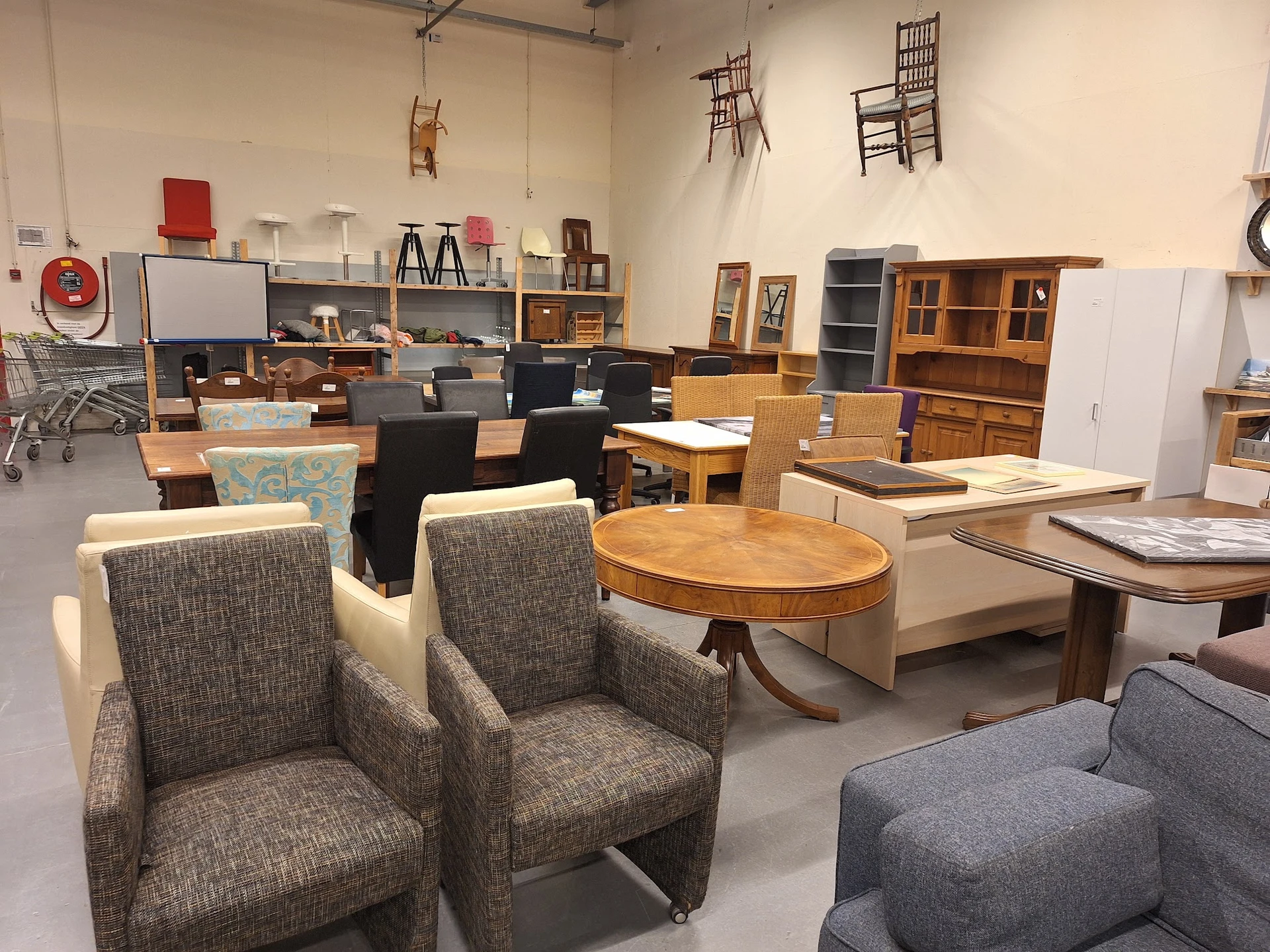 Winkelinterieur met tweedehands meubels: grijze stoelen, houten tafels, kasten en diverse inrichtingsstukken