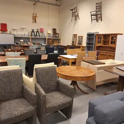 Winkelinterieur met tweedehands meubels: grijze stoelen, houten tafels, kasten en diverse inrichtingsstukken