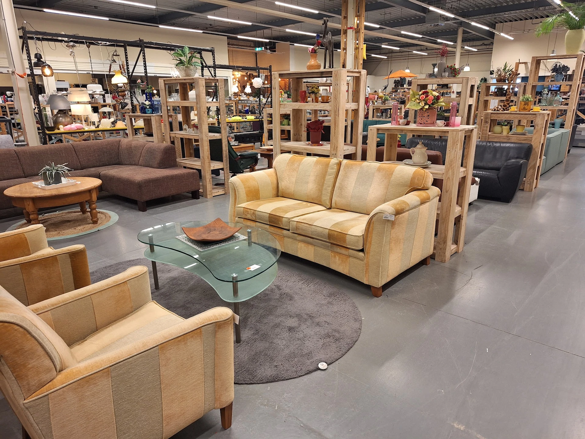 Winkelvloer met beige leren meubels, groene glazen tafel en houten bijzettafels in een grote ruimte met stellingen op de acht