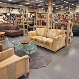 Winkelvloer met beige leren meubels, groene glazen tafel en houten bijzettafels in een grote ruimte met stellingen op de acht