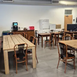 Kringloopwinkel-interieur met houten eettafels, stoelen en huisraad op achtergrond