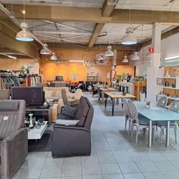 Ruim interieur van kringloopwinkel met zithoeken, tafels, stellingen en diverse meubels en spullen