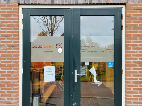 Donkergroene glazen winkeldeur met GoudGoed-logo en openingstijden op een bakstenen gevel