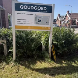 Informatiebord met openingstijden en adresgegevens, deels bedekt door begroeiing