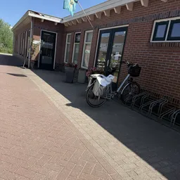 Voorkant van een bakstenen winkel met ingang, ramen en fietsen in een standaard ernaast