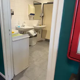 Ingang naar toiletruimte met twee wasbakken, prullenbak en tegelvloer
