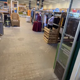 Winkelvloer van kringloopwinkel met kleding op rekken en hangers, enkele klantjes en meubels