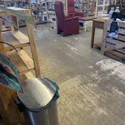 Winkelinterieur met betonnen vloer, houten meubels en diverse voorwerpen op de achtergrond