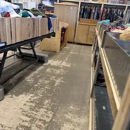 Betonnen winkelvloer met daglicht, stellingen en opgestapelde goederen in een kringloopwinkel