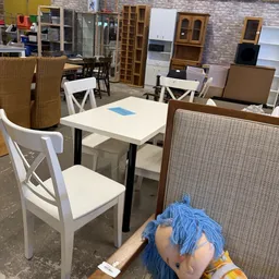 Winkelvloer met witte stoelen en tafels, stellingen met meubels en textielwaar op de achtergrond