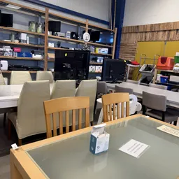 Winkelvloer met houten en beige stoelen, achter computers en stellingen met artikelen
