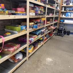 Houten stellingen gevuld met diverse tweedehands artikelen en speelgoed in een kringloopwinkel