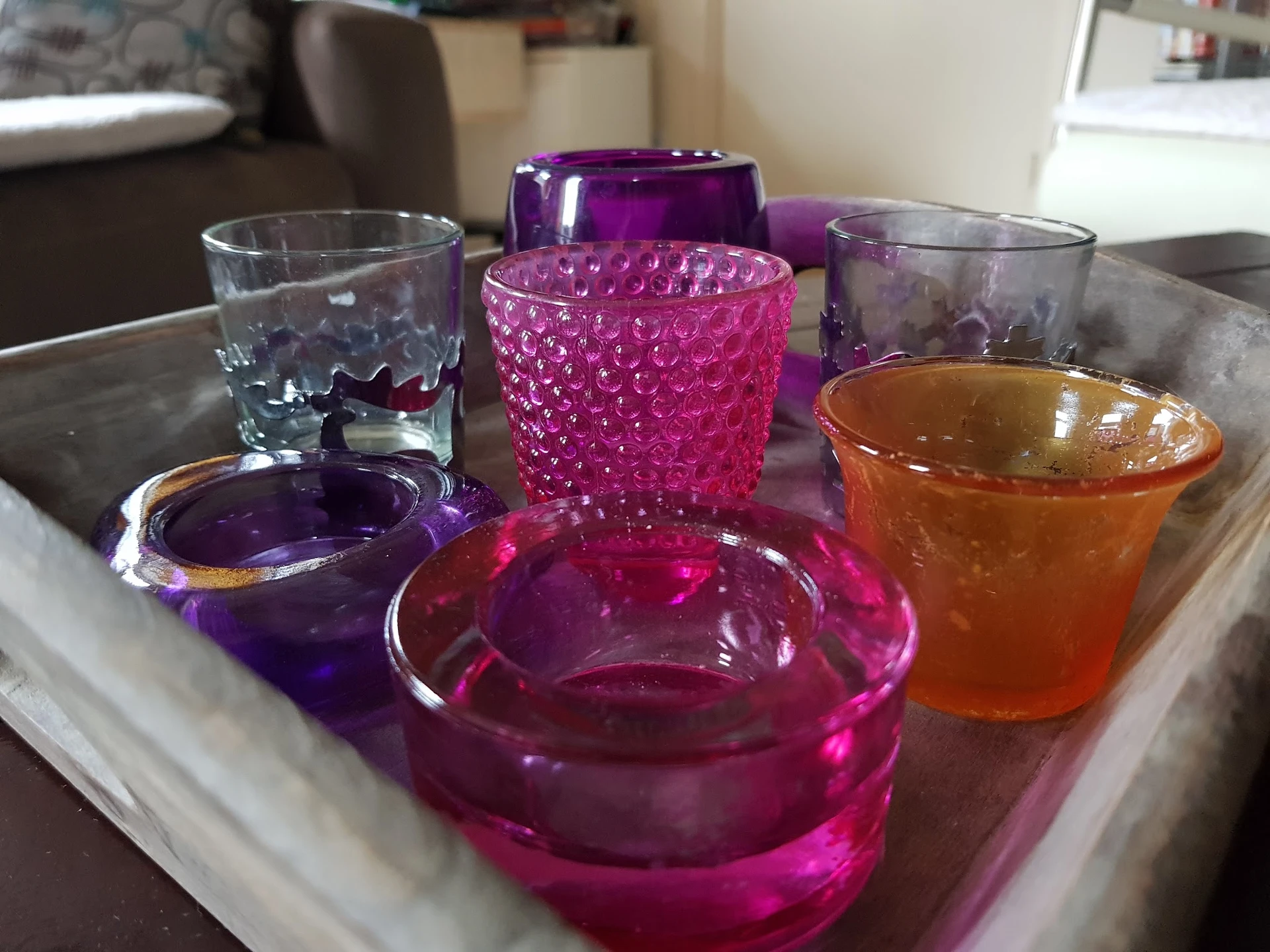 Verzameling gekleurde glazen schalen en kandelaars in paars, roze en oranje op een dienblad
