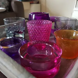 Verzameling gekleurde glazen schalen en kandelaars in paars, roze en oranje op een dienblad