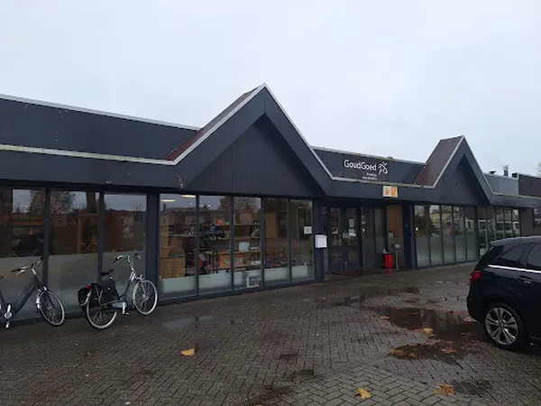 Gevel van kringloopwinkel met zwarte daklijsten, grote ramen, ingang en fietsen ervoor op een parkeerterrein