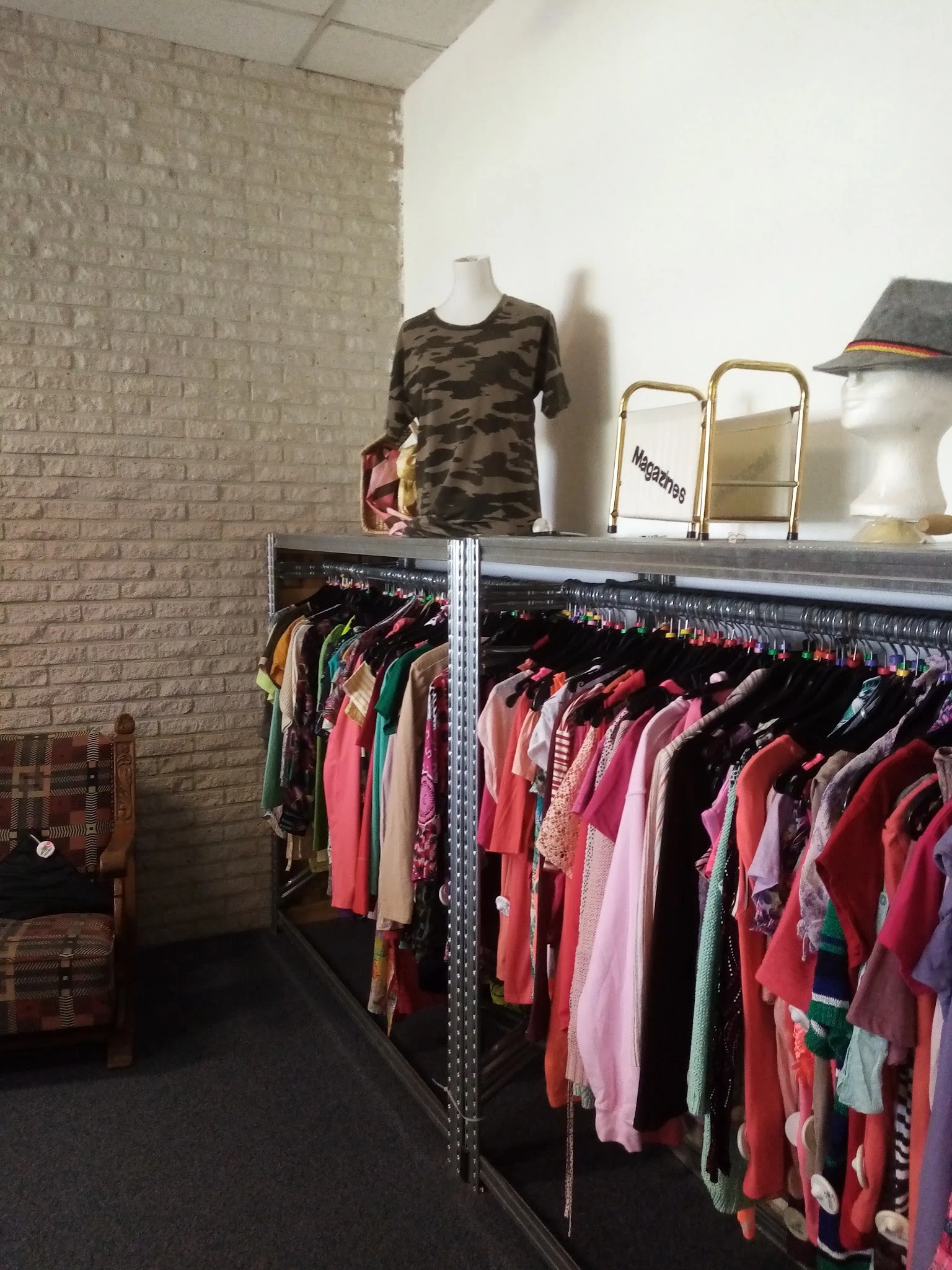 Rekken met tweedehands dameskleding in verschillende kleuren, met een etalagepop in camouflageprint bovenop