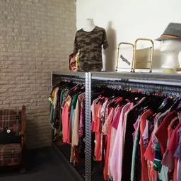 Rekken met tweedehands dameskleding in verschillende kleuren, met een etalagepop in camouflageprint bovenop
