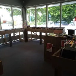 Winkelvloer met houten toonbanken en stellingen bij grote ramen met uitzicht op parkeerplaats