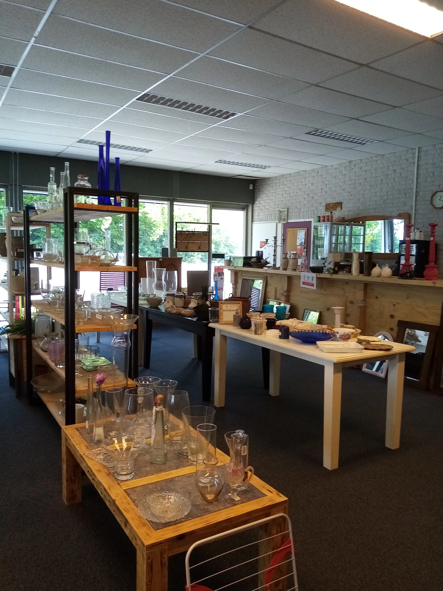 Winkelvloer met houten tafels, stellingen met servies, glaswerk en huishoudartikelen, natuurlijk licht van buiten