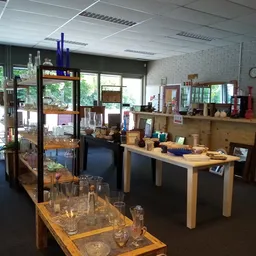 Winkelvloer met houten tafels, stellingen met servies, glaswerk en huishoudartikelen, natuurlijk licht van buiten