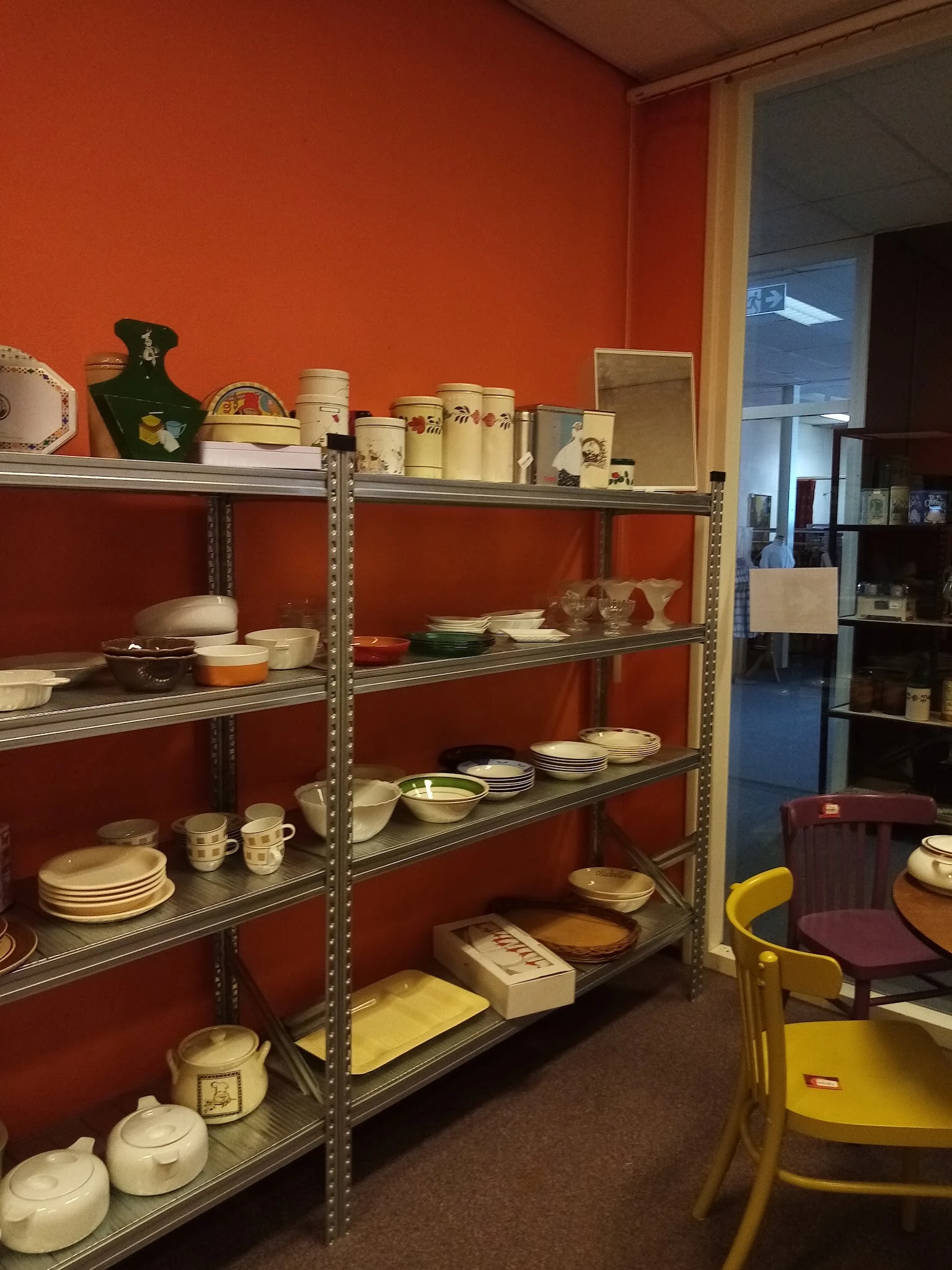 Metalen stellingen met servies, borden, schalen en huishoudartikelen tegen rode muur