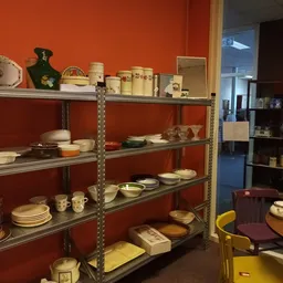 Metalen stellingen met servies, borden, schalen en huishoudartikelen tegen rode muur