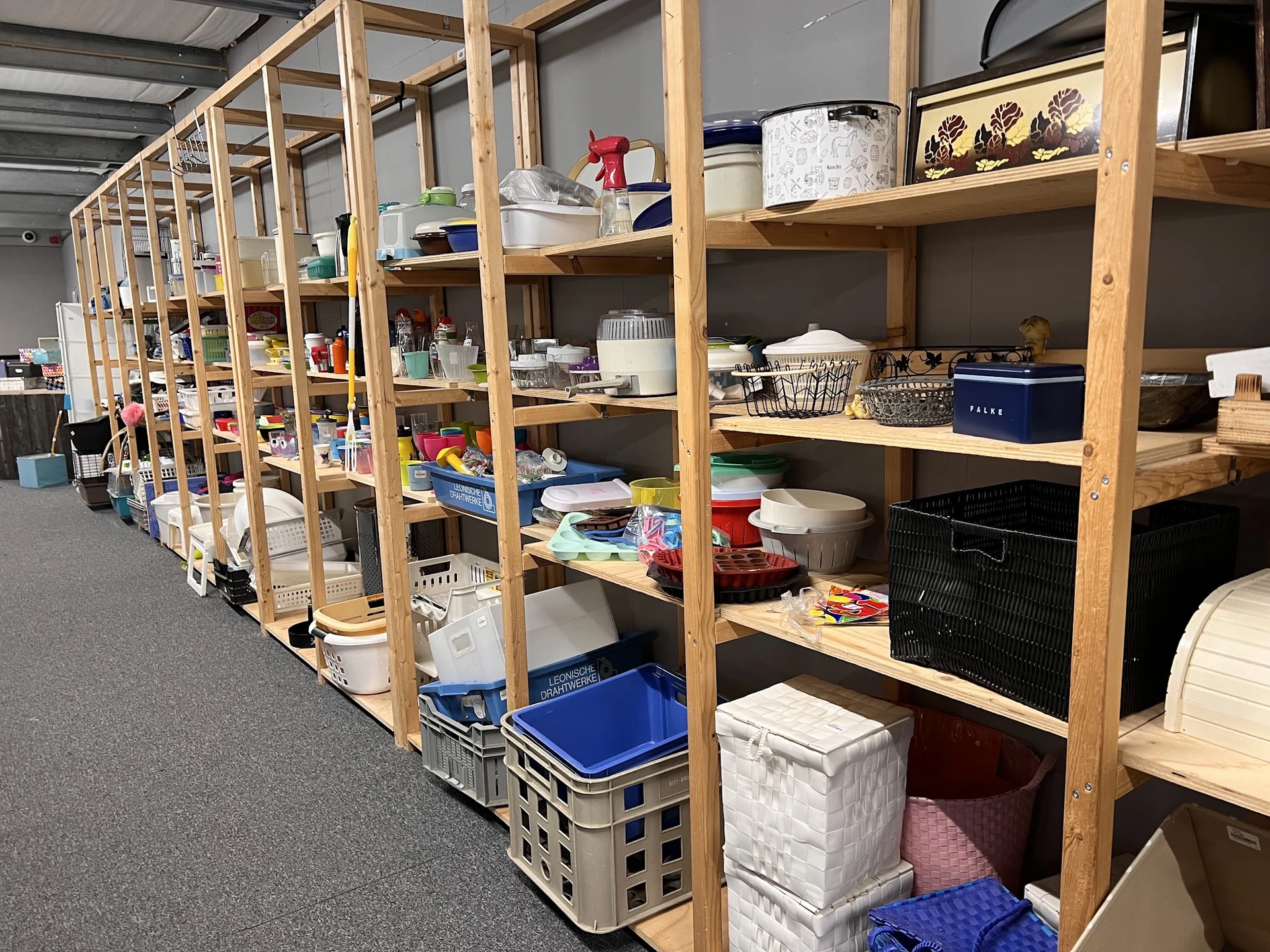Houten stellingskasten met diverse huishoudelijke spullen, dozen en opbergmaterialen in een kringloopwinkel.
