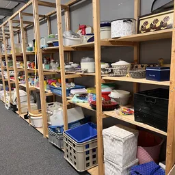 Houten stellingskasten met diverse huishoudelijke spullen, dozen en opbergmaterialen in een kringloopwinkel.