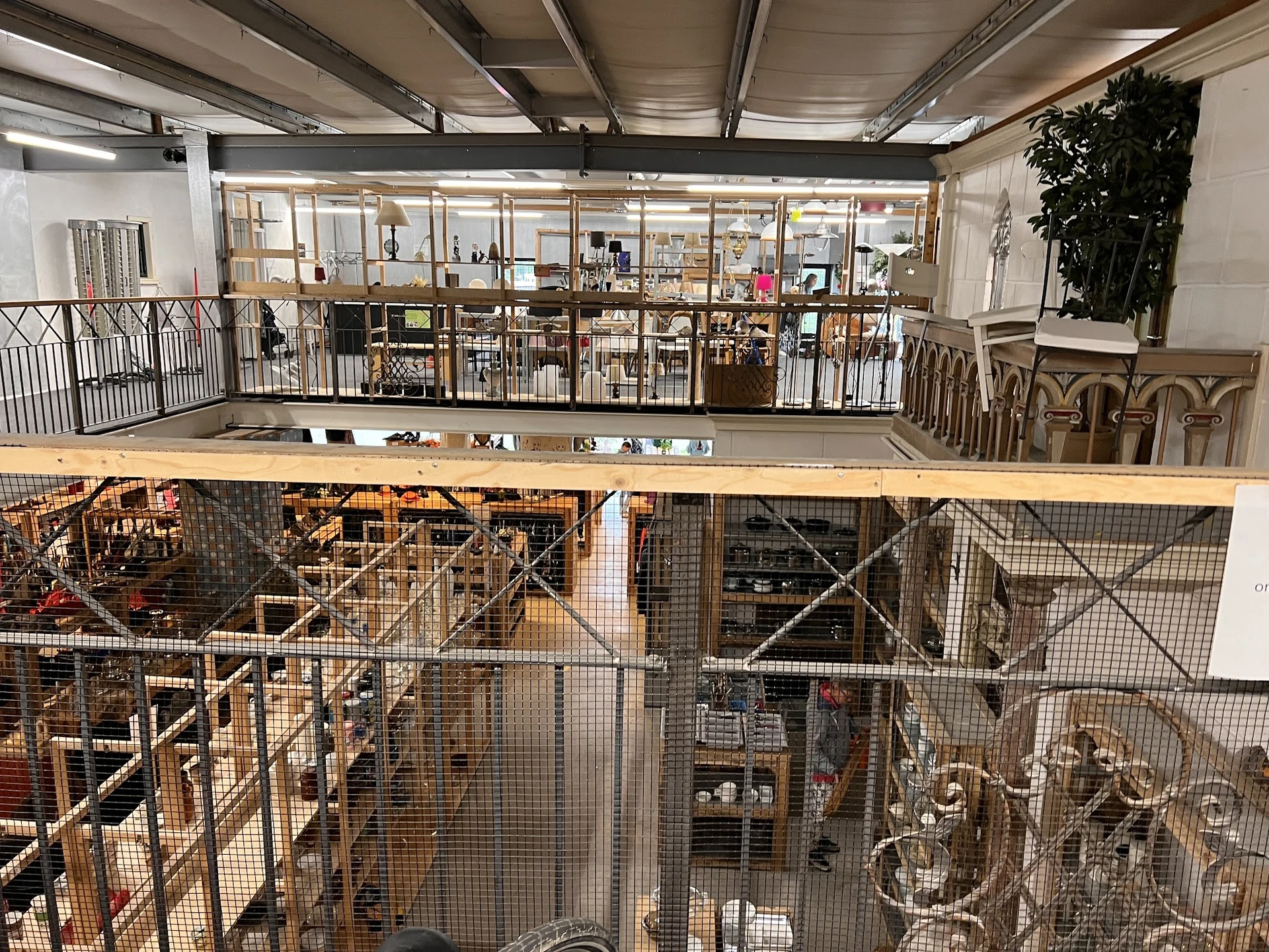 Tweelaags kringloopwinkel met geafschermde opslagruimtes, stellingen en diverse goederen zichtbaar