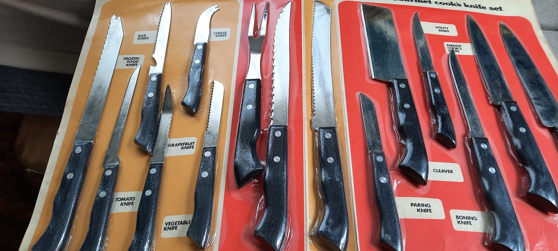 Uitgestalde messensets met zwarte handvatten op gele en rode achtergronden in de winkel