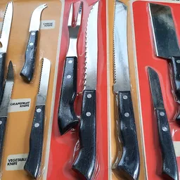 Uitgestalde messensets met zwarte handvatten op gele en rode achtergronden in de winkel
