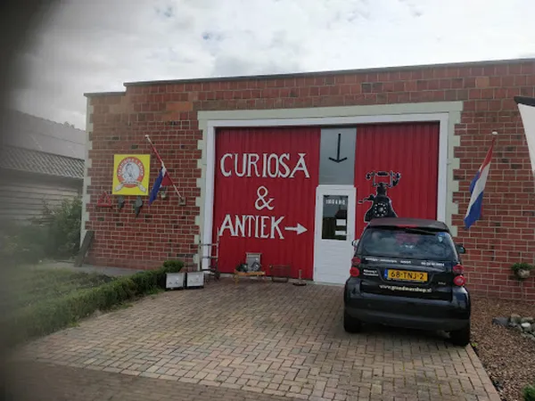 Rode gevel van kringloopwinkel met witte deuromlijsting en uithangbord 'Curiosa & Antiek', een auto geparkeerd ervoor