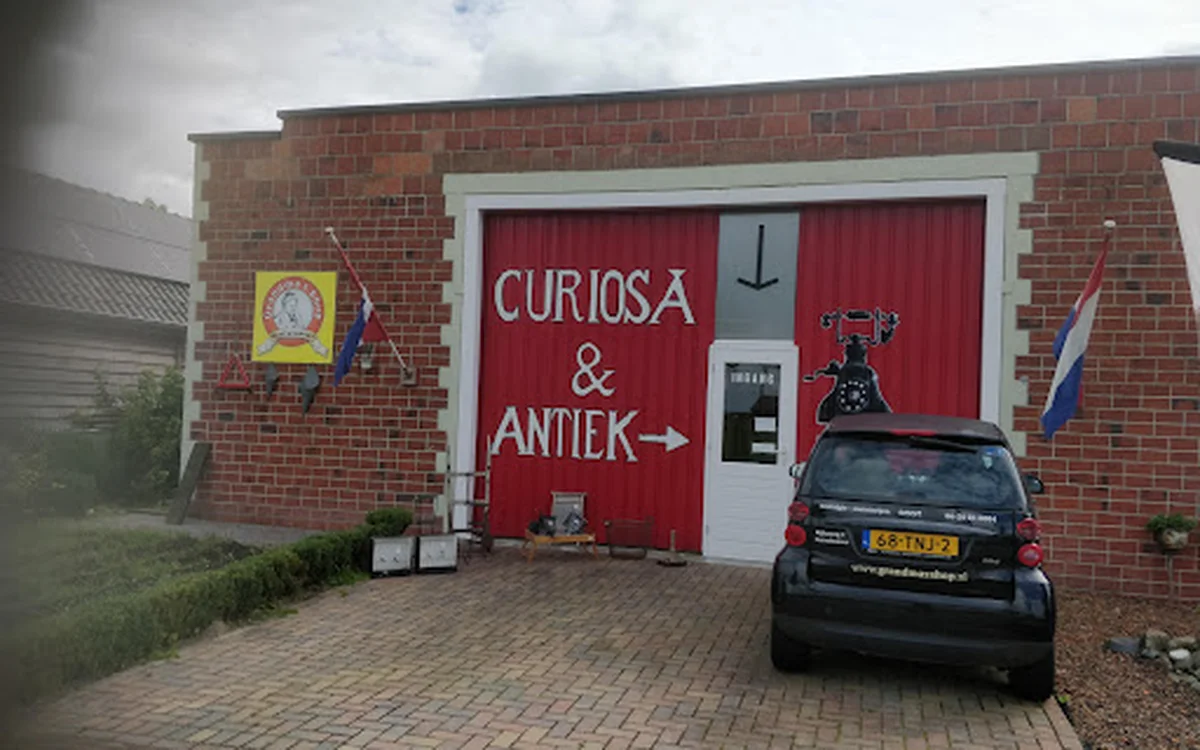 Rode gevel van kringloopwinkel met witte deuromlijsting en uithangbord 'Curiosa & Antiek', een auto geparkeerd ervoor