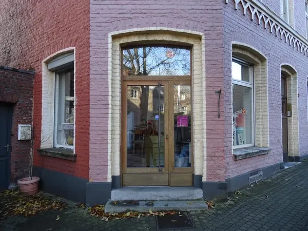 Voorgevel van kringloopwinkel met rode bakstenen muur, grote houten deuren met glas en ramen met stenen omlijsting