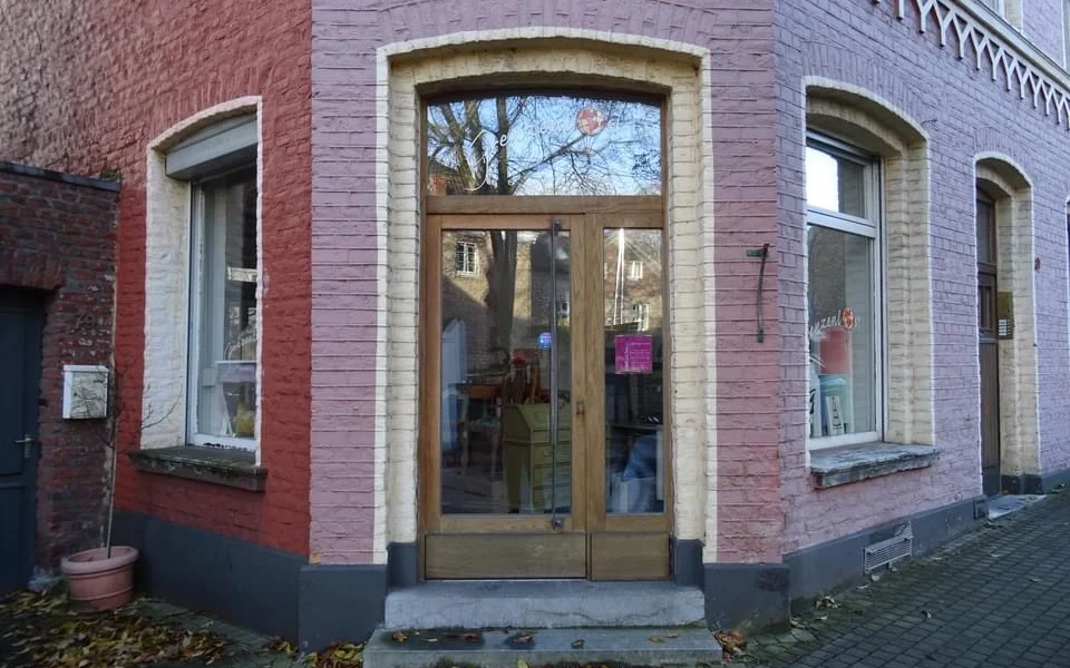 Voorgevel van kringloopwinkel met rode bakstenen muur, grote houten deuren met glas en ramen met stenen omlijsting