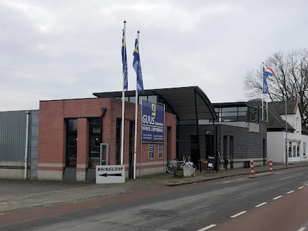 Voorgevel van kringloopwinkel met rode bakstenen muur, moderne aanbouw, blauwe vlaggen en uithangbord aan straat