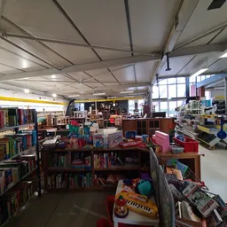 Overzicht van de winkelvloer met boekenrekken, speelgoed, kleding en diverse tweedehands artikelen onder fluorescente verlich