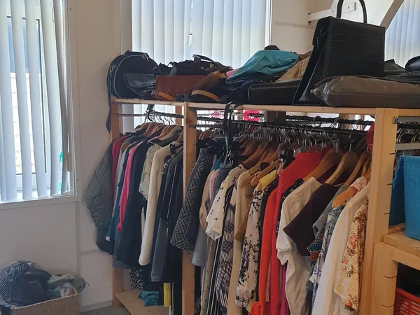Rekken met tweedehands kleding in verschillende kleuren, daarop gestapelde tassen en spullen op de bovenste plank