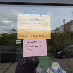 Openingstijden bord met handgeschreven notitie eronder op een raam