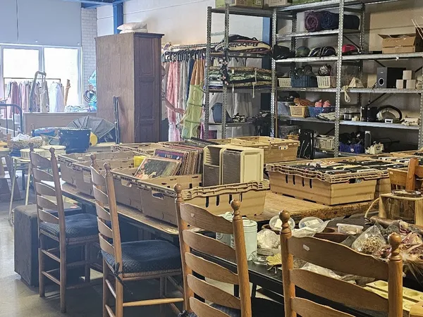 Winkelvloer met houten stoelen, gele kunststofkratten, stellingen met kleding en huishoudartikelen