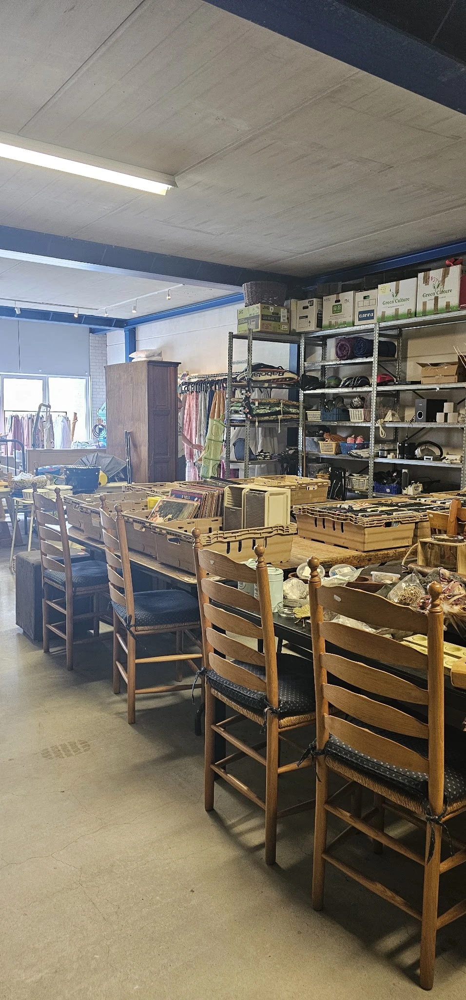 Winkelvloer met houten stoelen, gele kunststofkratten, stellingen met kleding en huishoudartikelen