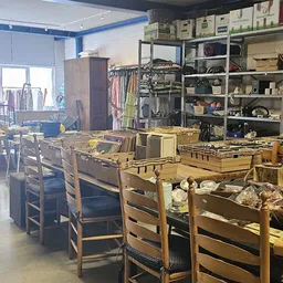 Winkelvloer met houten stoelen, gele kunststofkratten, stellingen met kleding en huishoudartikelen