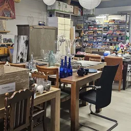 Winkelbinnenruimte met houten tafels, stoelen, blauwe flessen, serviesgoed en schappen vol spullen op de achtergrond