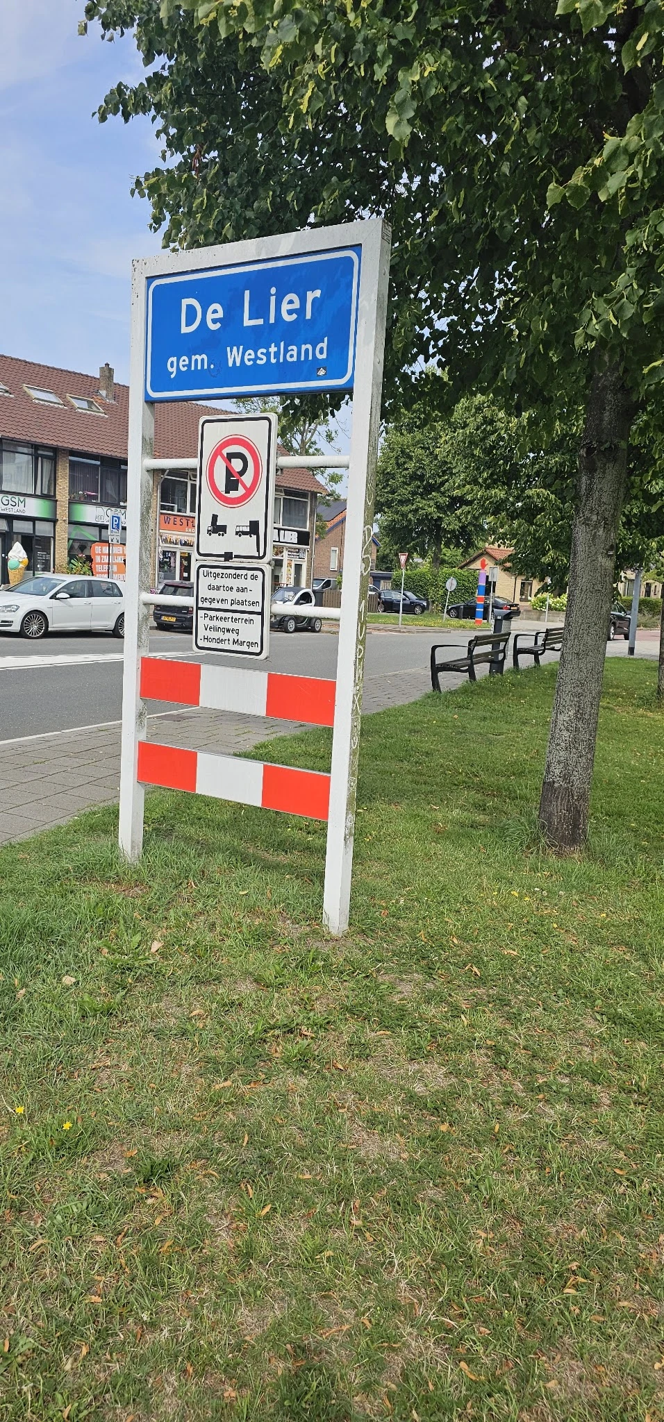 Witte paal met rode-witte waarschuwingsstrepen en bord in gras naast straat