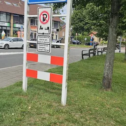 Witte paal met rode-witte waarschuwingsstrepen en bord in gras naast straat